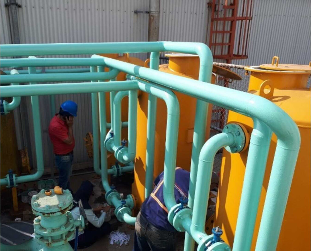 Montaje del sistema de filtración de 100 gpm: filtros amarillos y tubería verde agua, con dos técnicos trabajando en las válvulas.