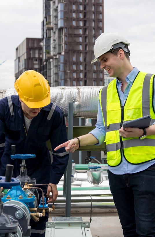 Dos técnicos de Watercol revisando las válvulas de un sistema de tratamiento de agua en una terraza industrial.